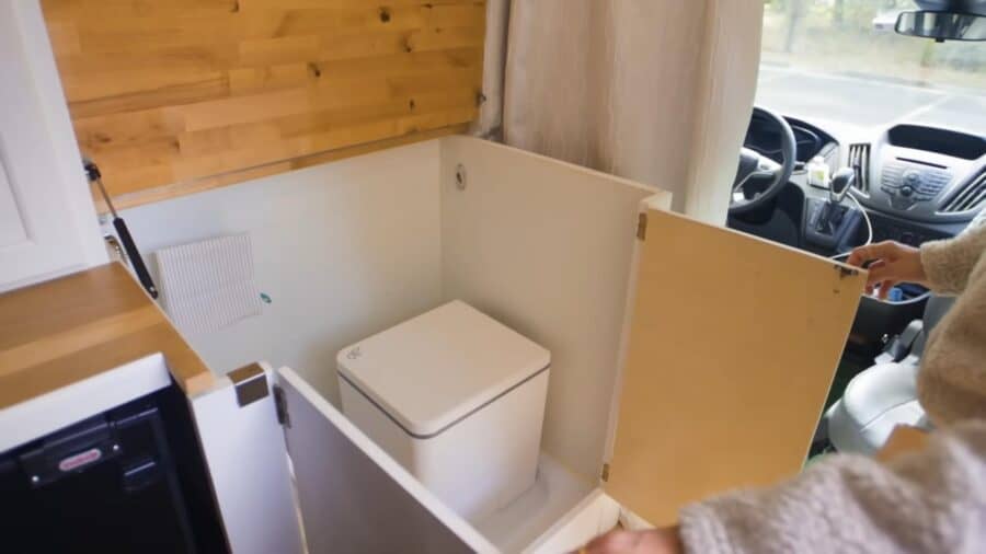 Compact tiny house bathroom with portable toilet and wooden accents.
