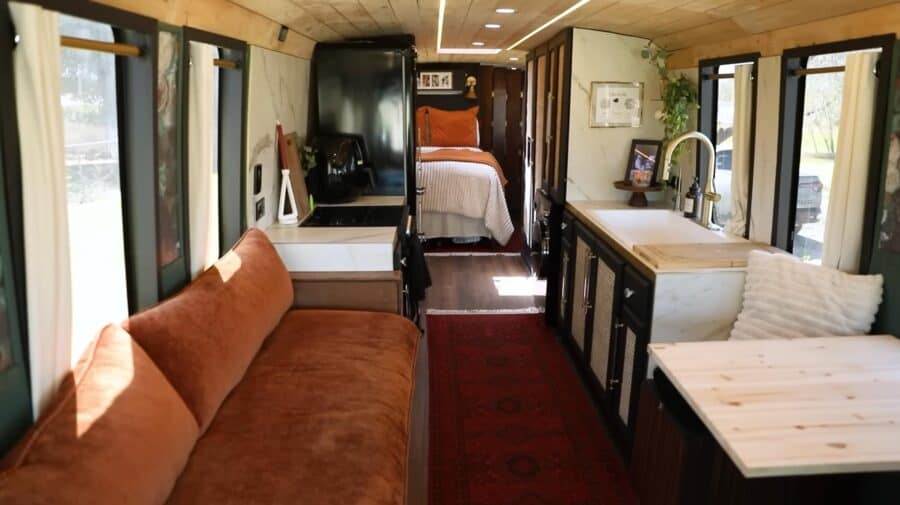 Compact Skoolie living space with a cozy sofa and functional kitchen area.