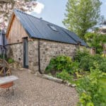Charming tiny stone house with a metal roof and lush garden in a peaceful setting.