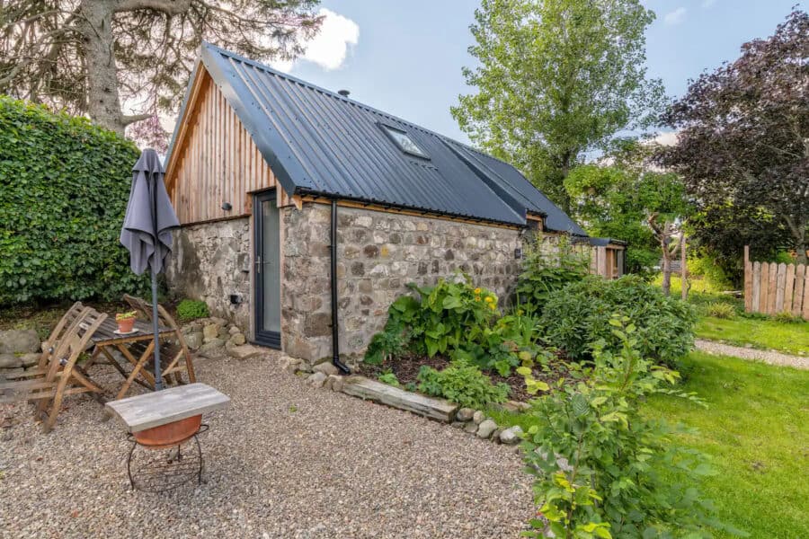 Charming tiny stone house with a metal roof and lush garden in a peaceful setting.
