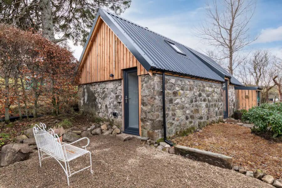 Charming tiny stone house featuring a metal roof and wooden accents, nestled in a natural setting wi.