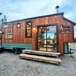 Small wooden tiny house with large glass door and outdoor steps, built with locally-milled wood.