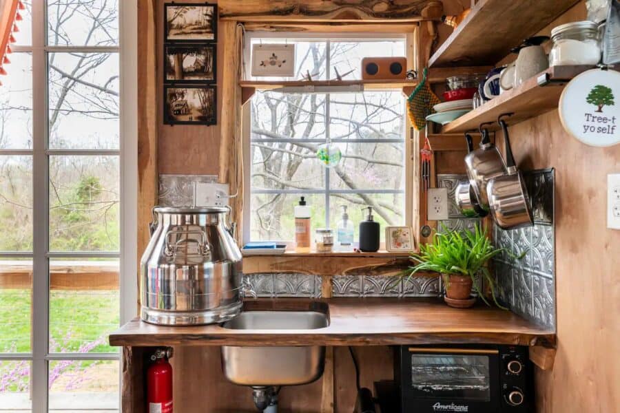 Charming tiny house kitchen with wooden accents and large window overlooking nature.