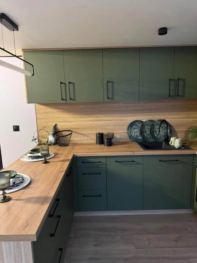 Sage-green kitchen in the Jake modular house with wood countertops, a wood backsplash, and black fixtures