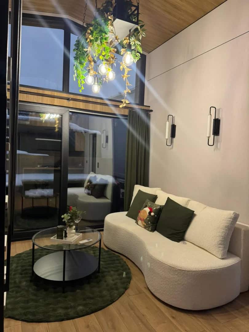 Double-height living room in the Jake modular house with a curved cream sofa and an arched glass gable window