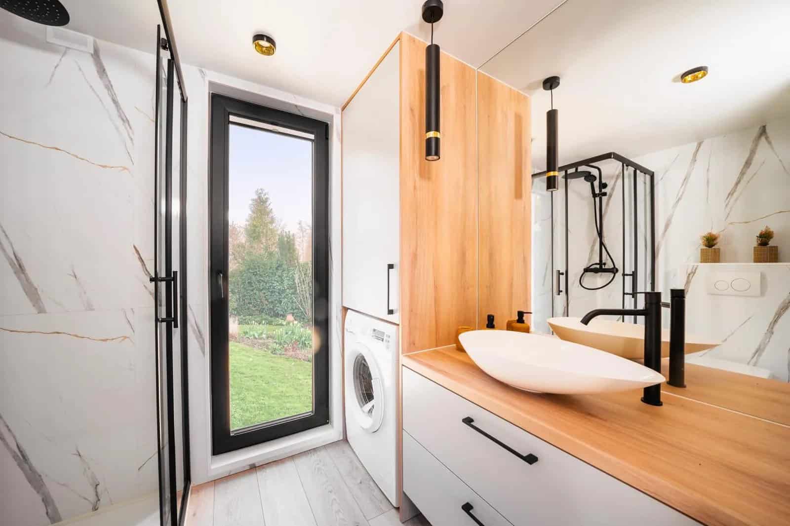 Marble-tiled bathroom in the Lukas modular house with a vessel sink, glass shower, and a built-in washing machine