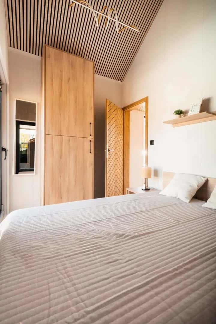 Ground-floor bedroom in the Lukas modular house with a wood wardrobe and slatted ceiling accent