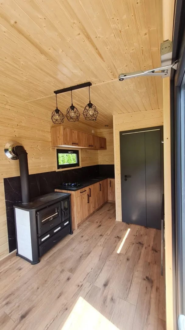 Spruce-lined interior of the Off-Grid Craft House with kitchenette, wood stove, and wall-mounted TV