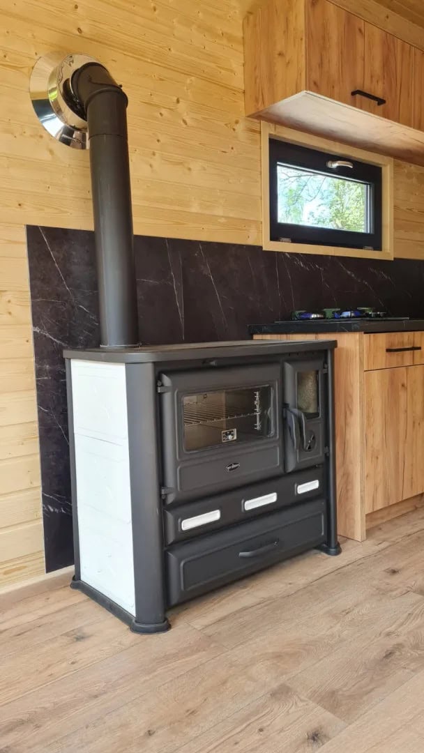 Wood-burning cook stove with oven against a dark tiled backsplash inside the Off-Grid Craft House