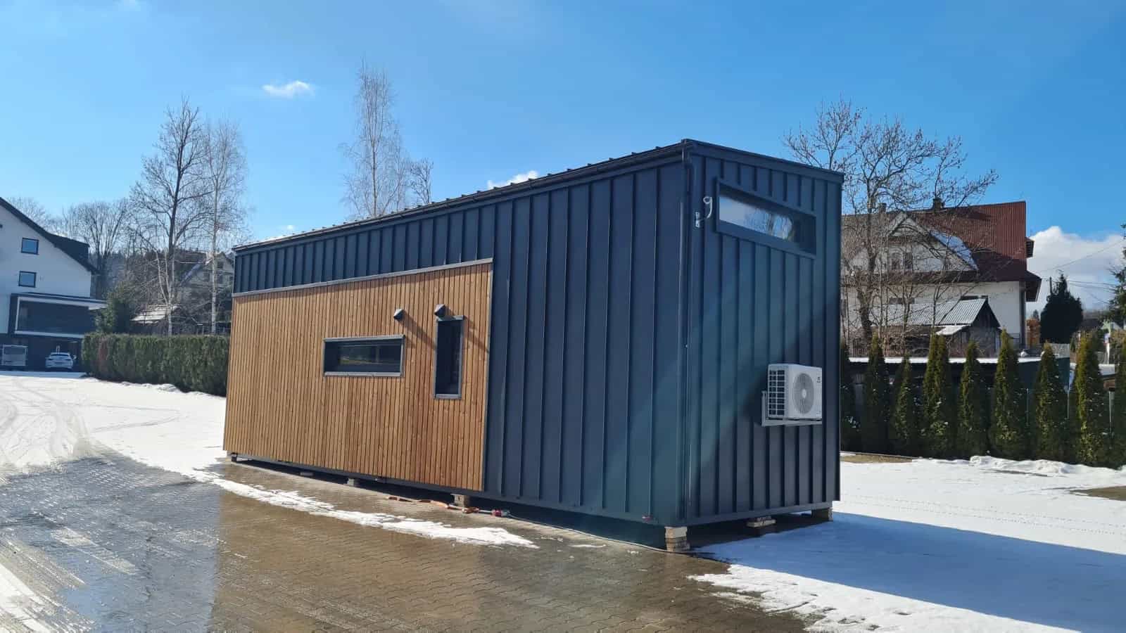 Side view of the Samuel modular house showing charcoal metal cladding, a wood accent, and an exterior AC unit
