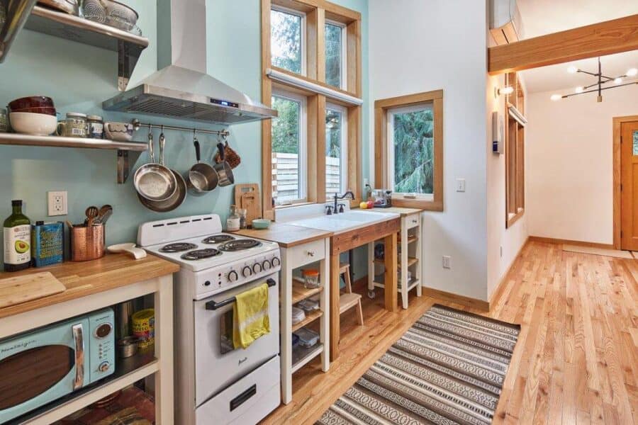 Efficient tiny house kitchen with natural wood accents and large windows for bright, open living.