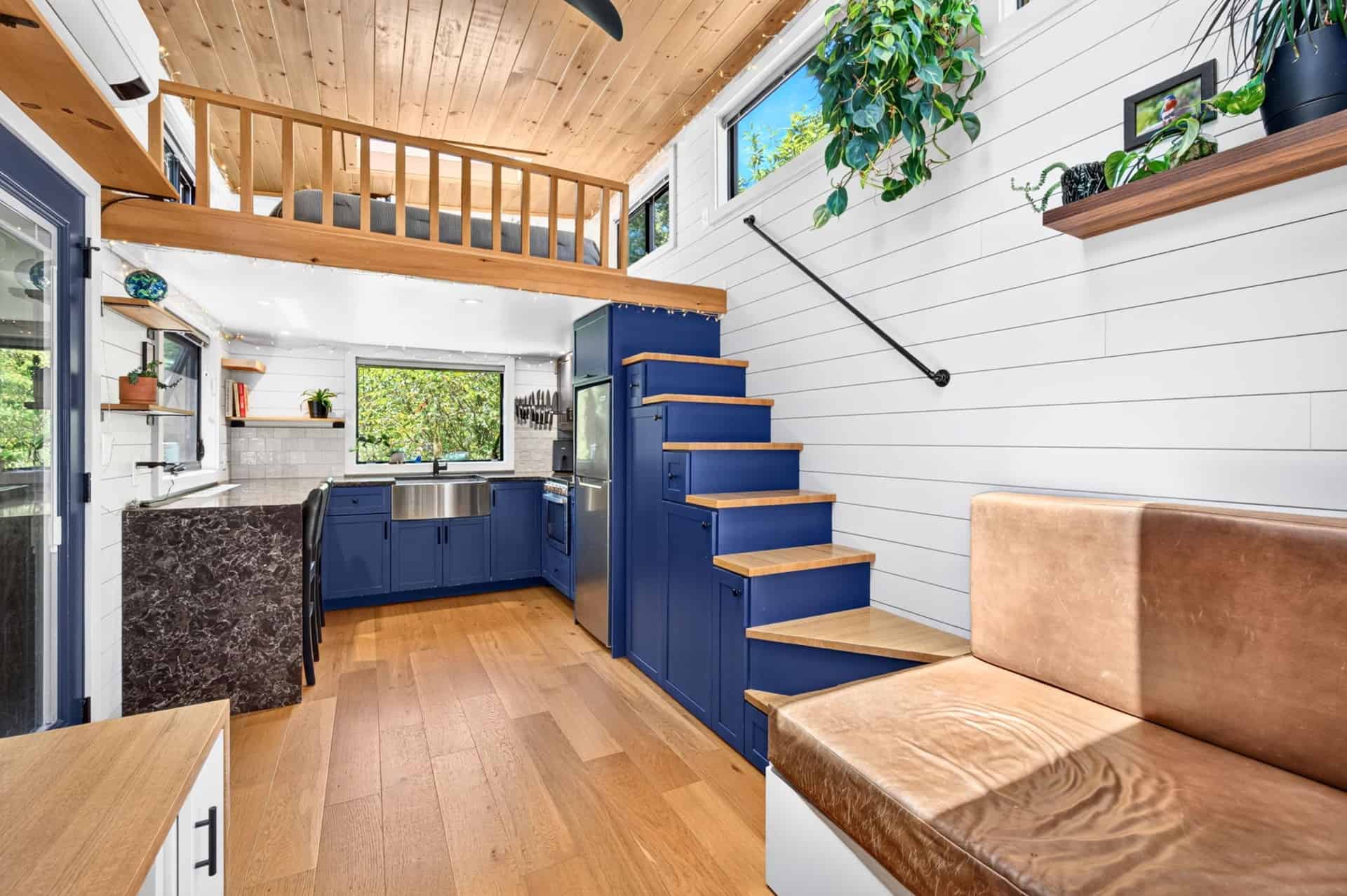 Bright tiny house interior with leather sofa, loft ladder, and wood ceiling
