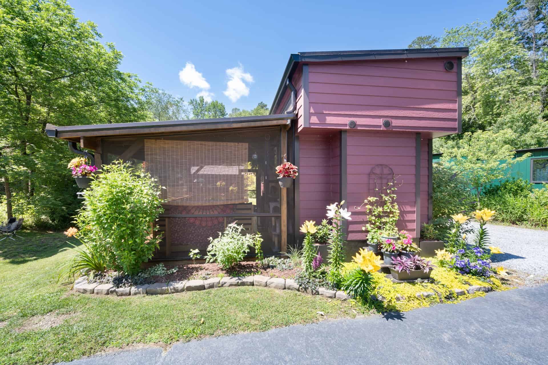 Front view of the plum tiny house with screened porch and flower gardens