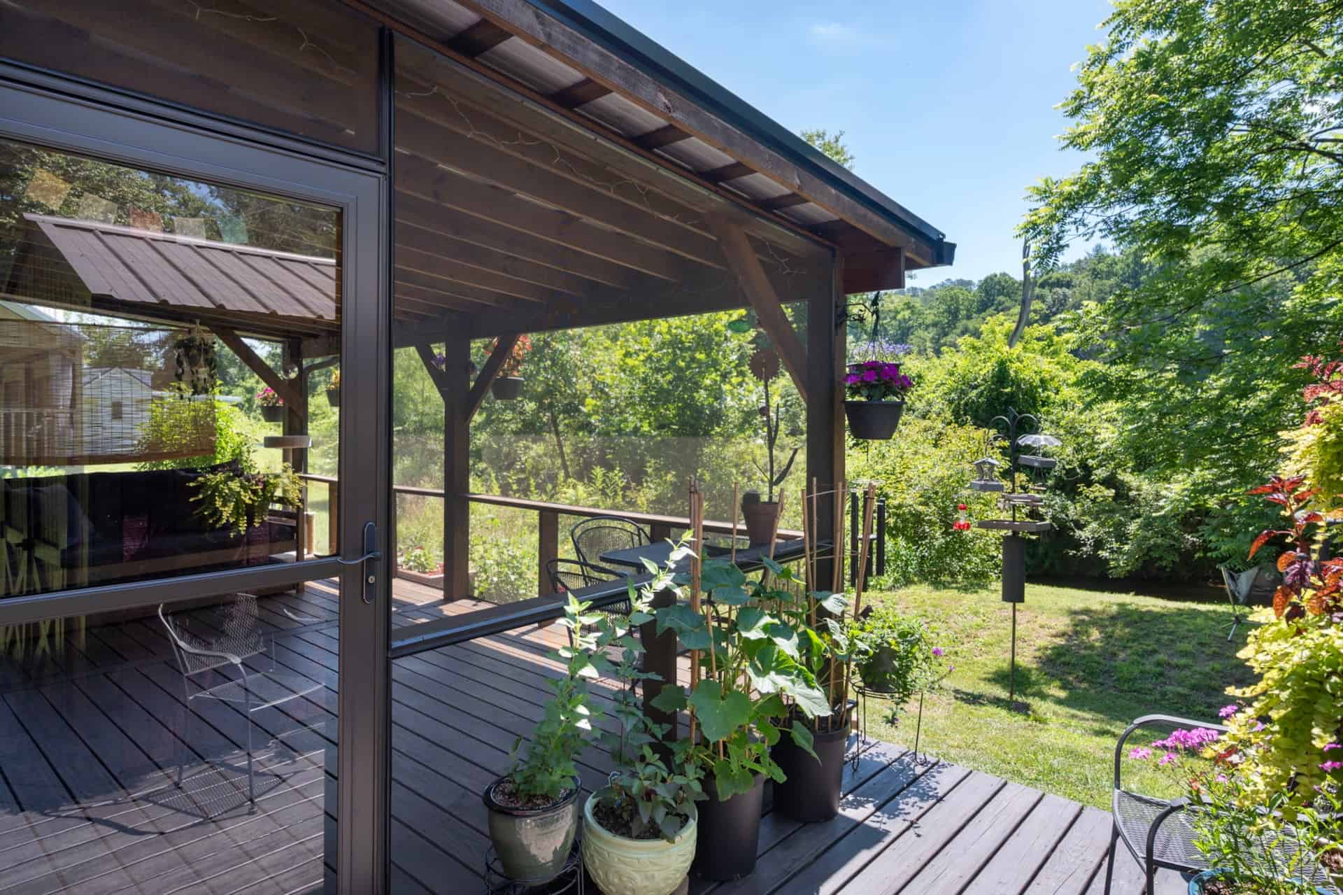 Screened porch corner filled with potted plants overlooking the green yard
