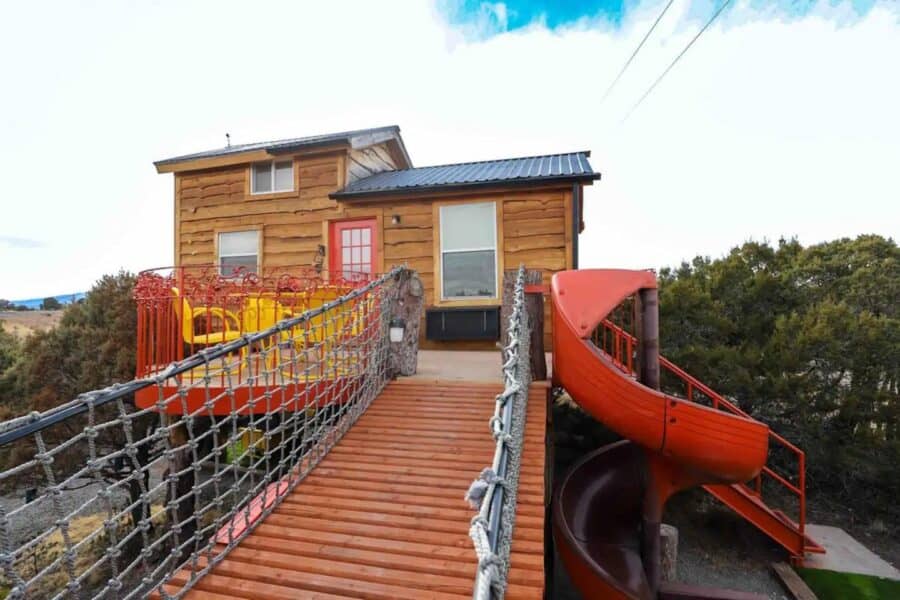 Treehouse with a red spiral slide and wooden bridge, set in a natural outdoor environment.