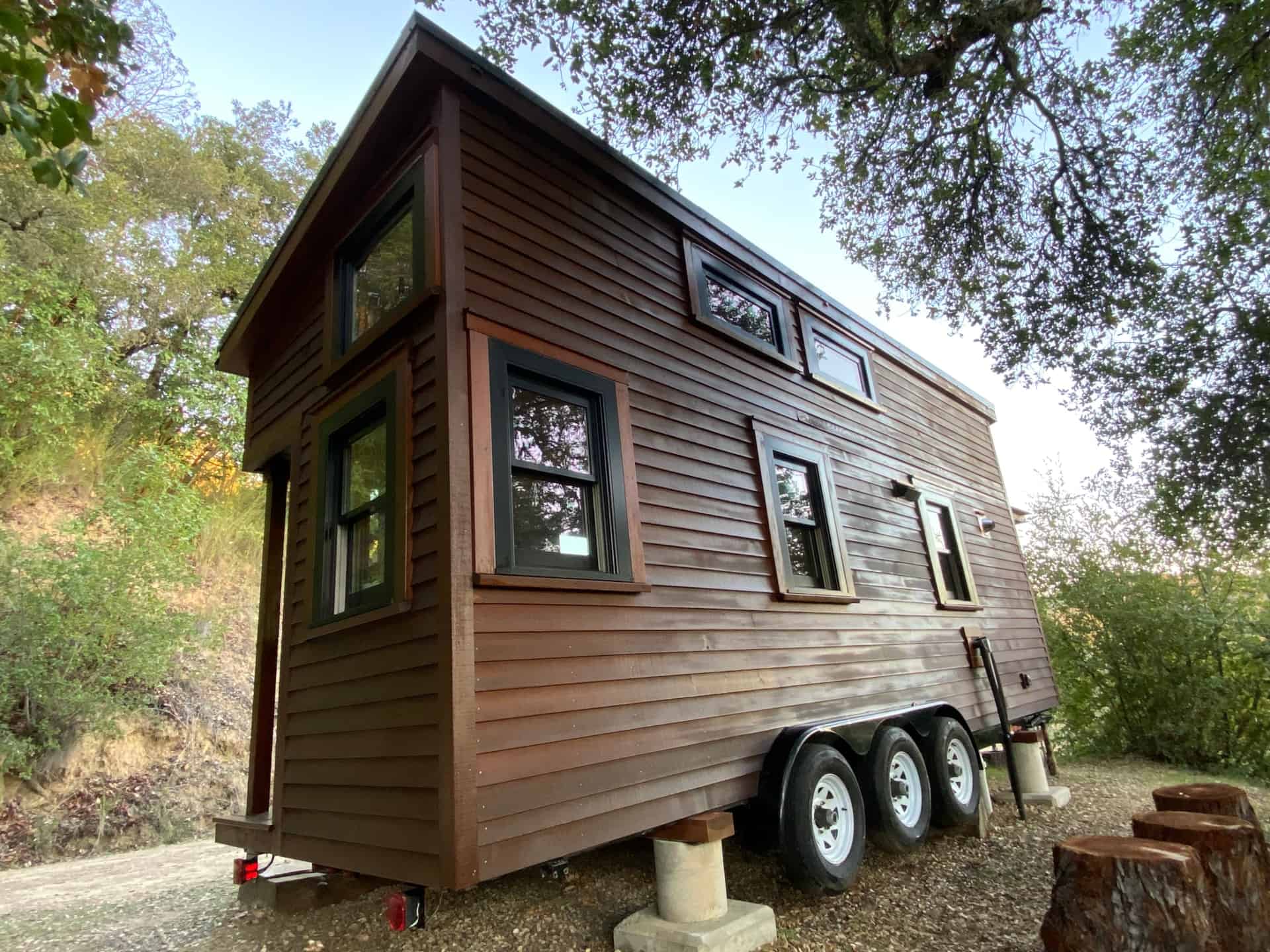Rear exterior view of the 24ft tiny house showing triple axle B-Wise trailer and loft windows