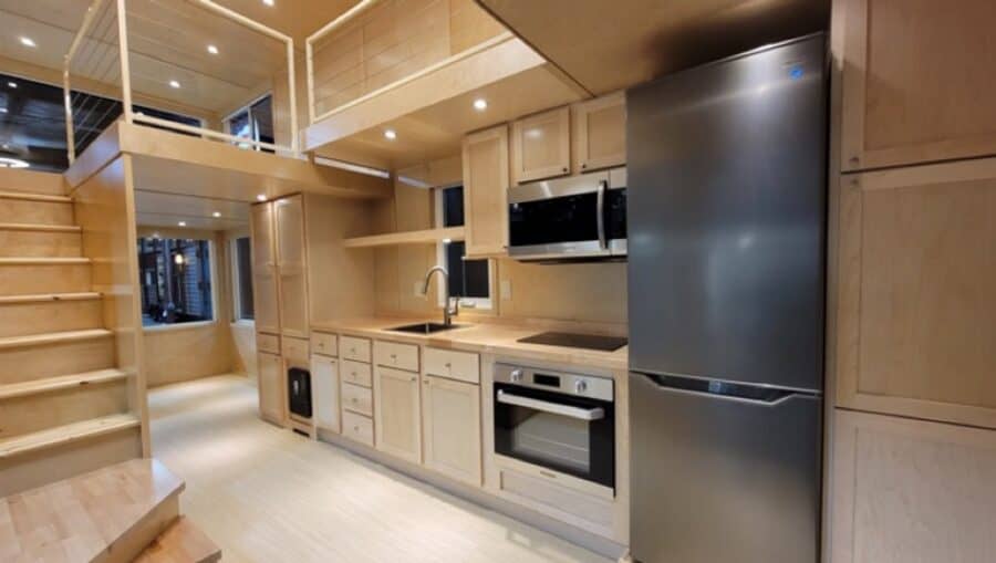 Modern tiny house kitchen with upgraded entertainment center and sleek appliances.