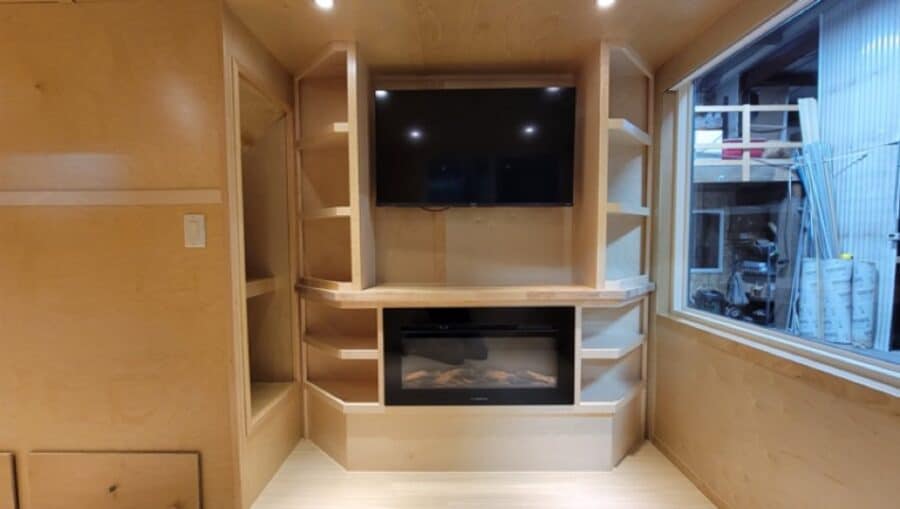 Entertainment center with TV and upgraded fireplace in tiny house interior.