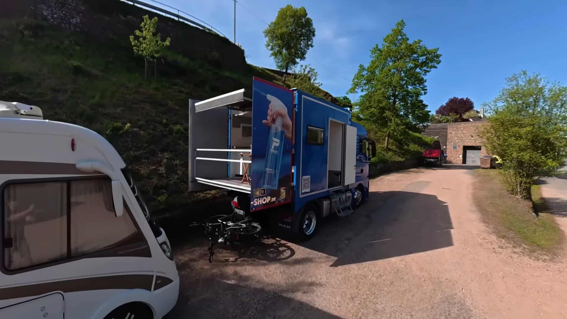 Wide view of the semi-truck tiny house with balcony fully deployed at campsite next to standard motorhome