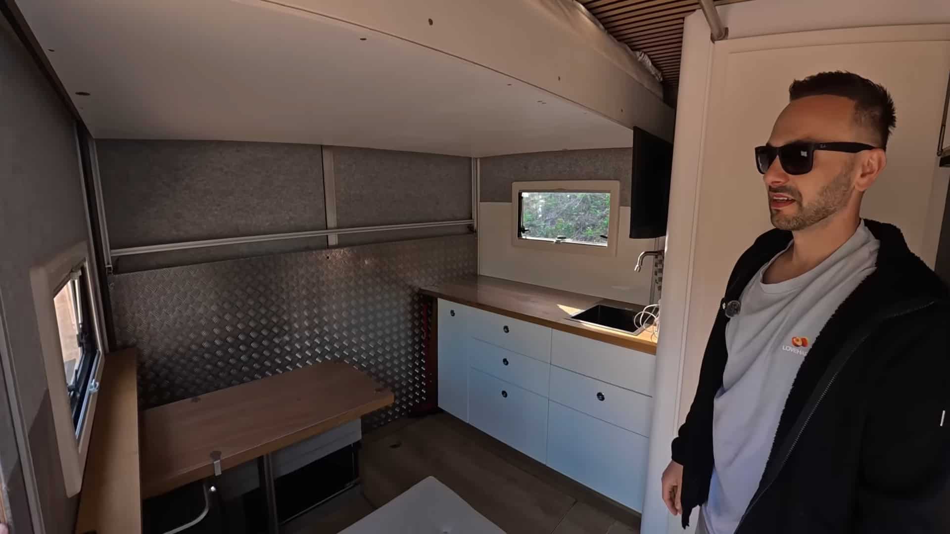Interior of the DIY semi-truck tiny house showing kitchen cabinetry, dining table, and elevator bed above