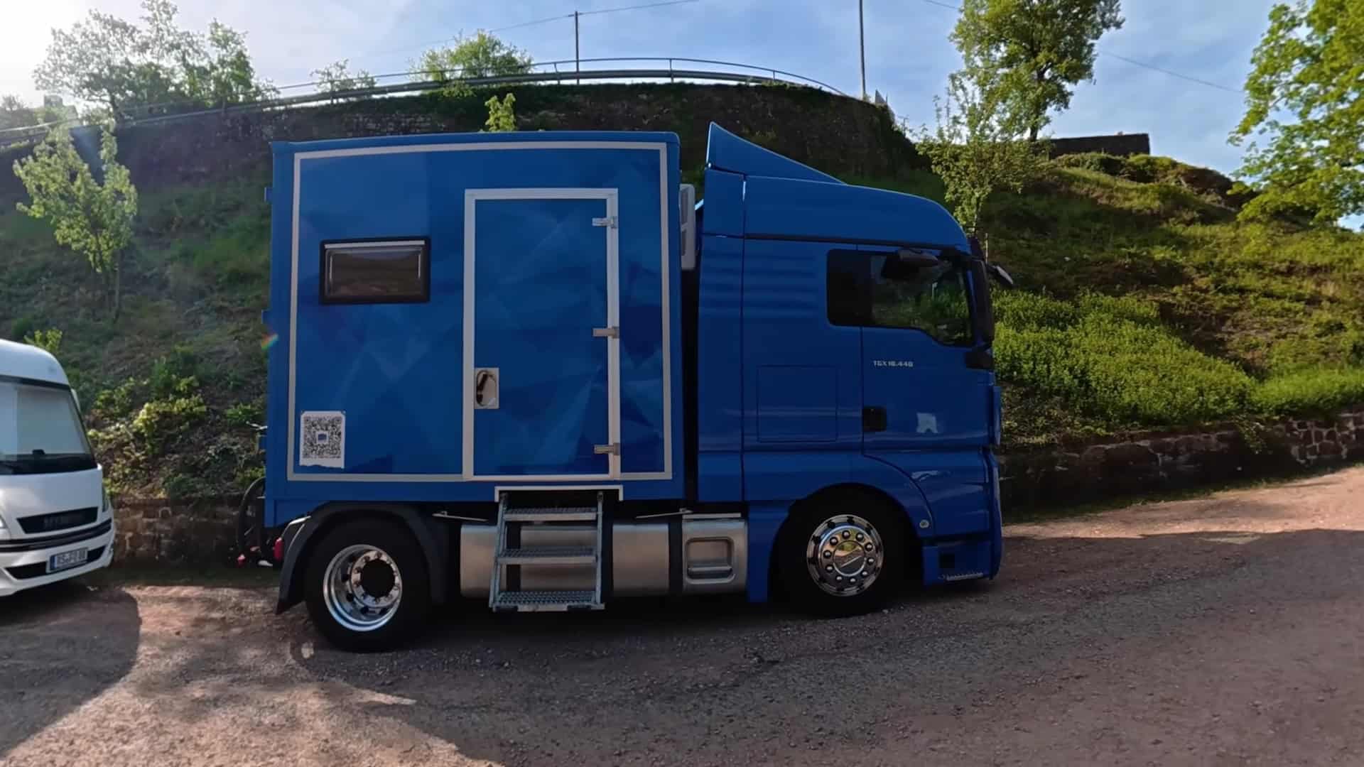 DIY semi-truck tiny house conversion MAN truck blue exterior with custom cargo box parked at campsite