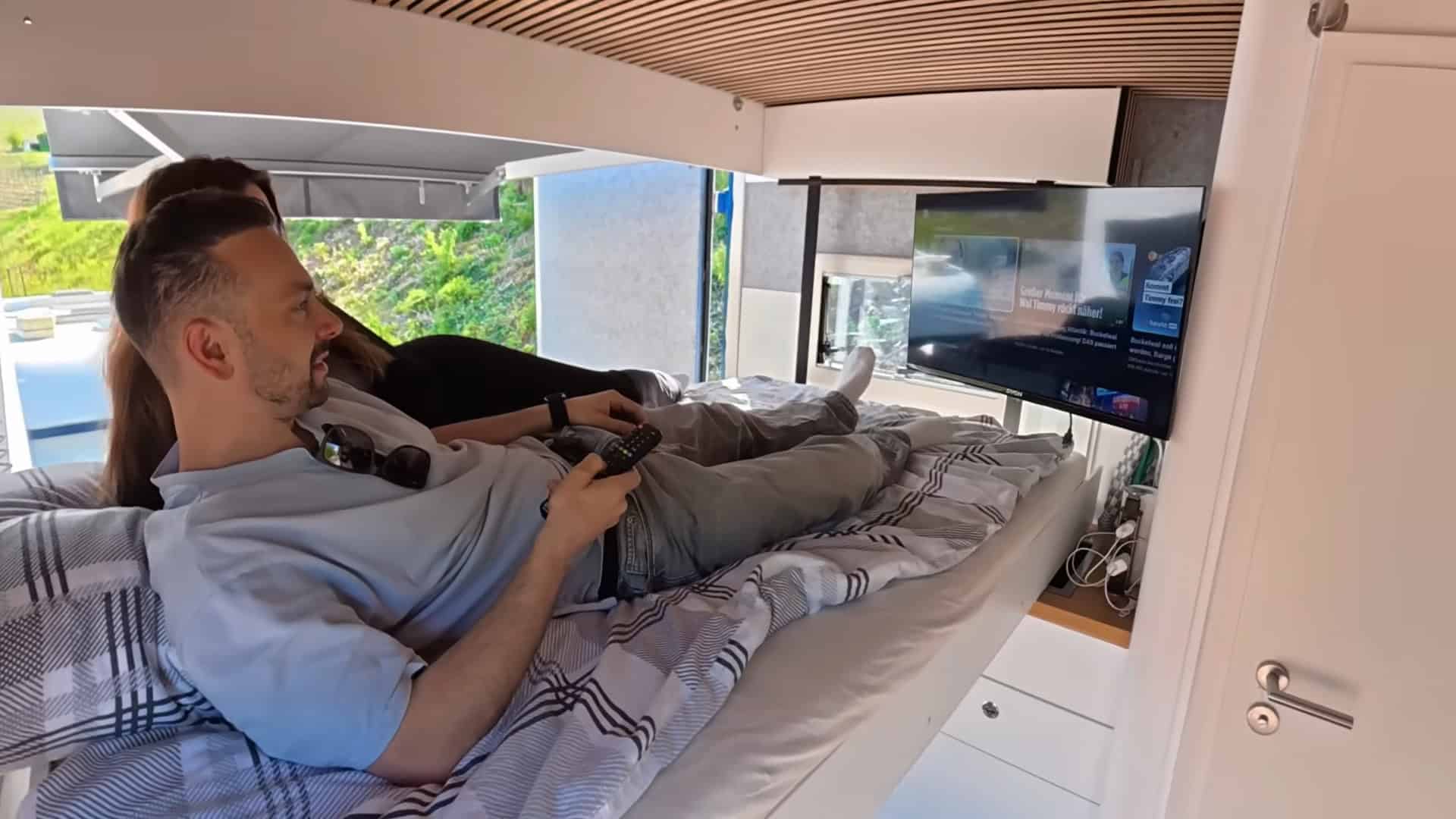 Waldemar relaxing on the lowered bed watching TV in the converted semi-truck tiny house