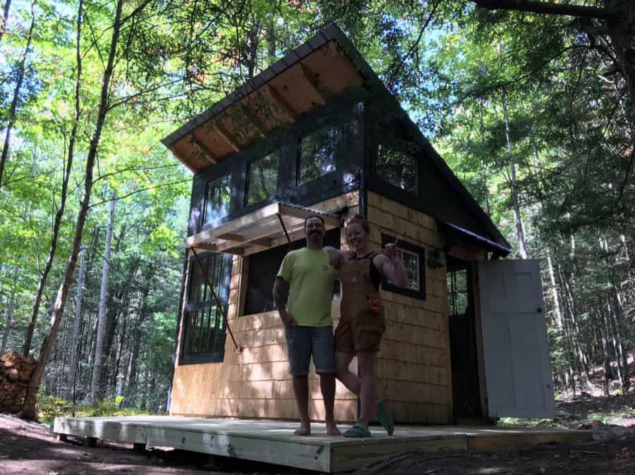 Small modern tiny house with large windows in wooded forest setting.