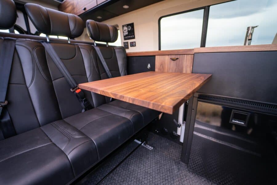 Interior of a family van converted into a tiny home with a foldable table and seating.