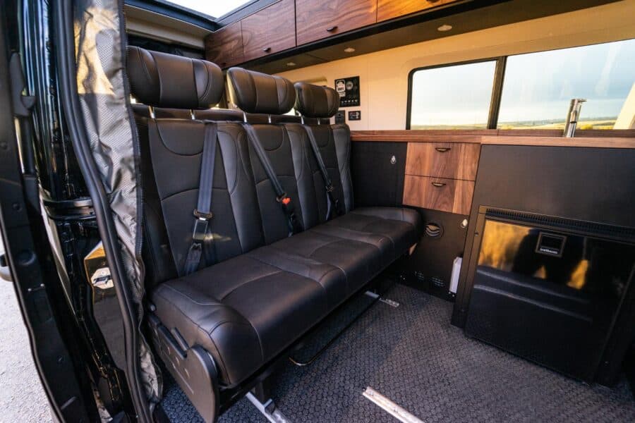 Interior of a family van converted into a tiny home with black seating and wooden accents.