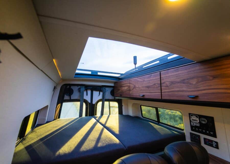 Interior view of a family van converted into a tiny home with a sleeping area and skylight.