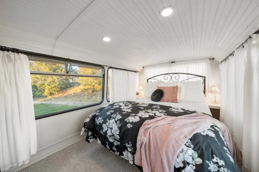 Cozy tiny house bedroom featuring a large window, floral bedding, and soft lighting for small space.