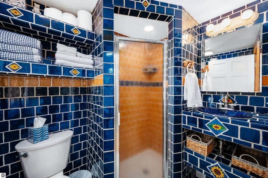 Bright blue tiled bathroom with a walk-in shower, white fixtures, and decorative accents in a small.