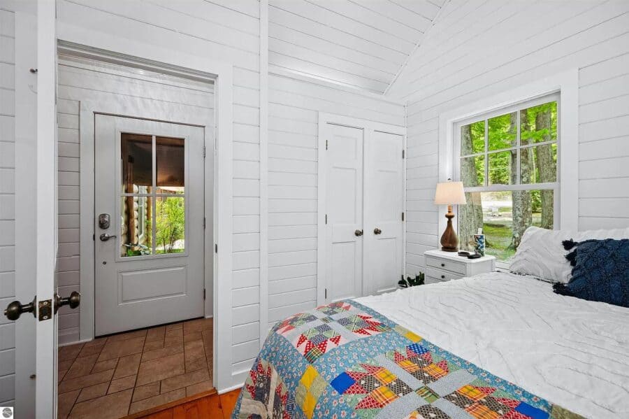 Interior view of a cozy log cabin bedroom with white walls, a bed with colorful quilt, and natural l.