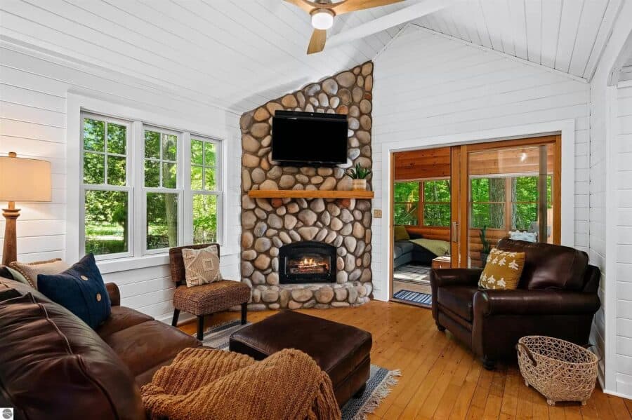 Inviting log cabin living room with stone fireplace and large windows in Northern MI.