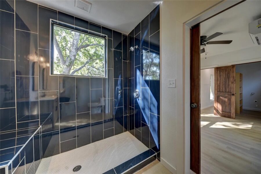 Modern shipping container home bathroom with sleek black tiles and large window.