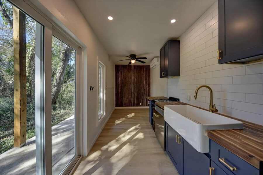 Modern tiny house kitchen with blue cabinets and large windows for natural light.