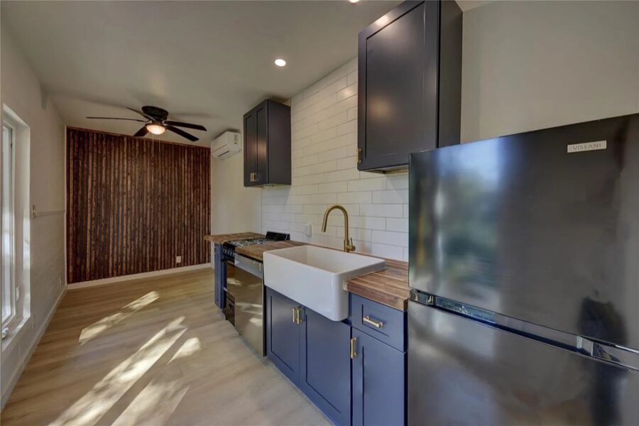 Modern tiny house kitchen with blue cabinets, farmhouse sink, and white subway tile backsplash.