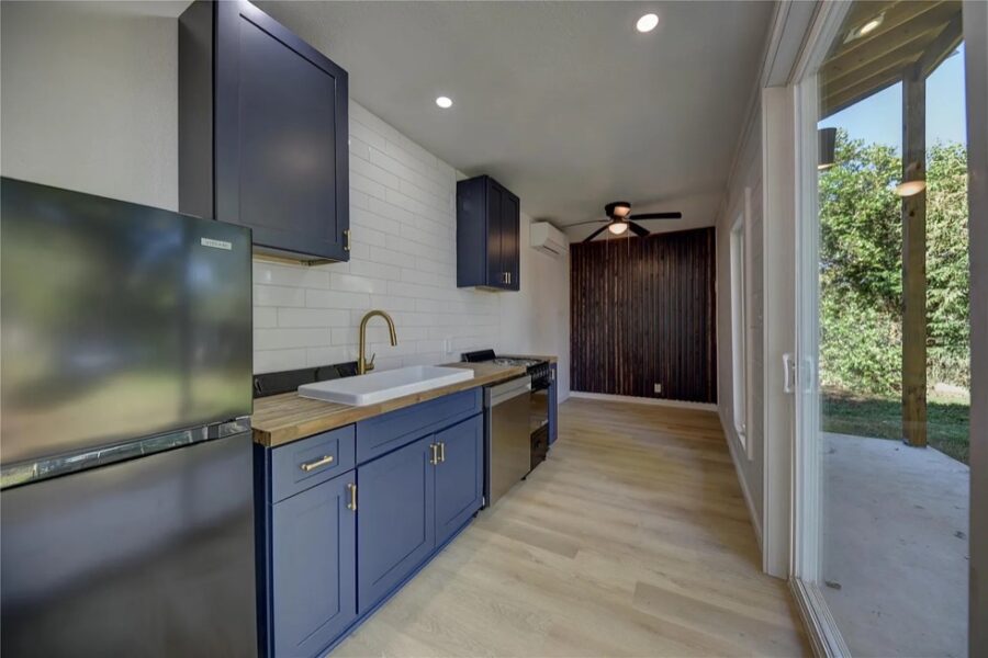 Modern tiny house kitchen with blue cabinets, white backsplash, and large sliding glass door for nat.