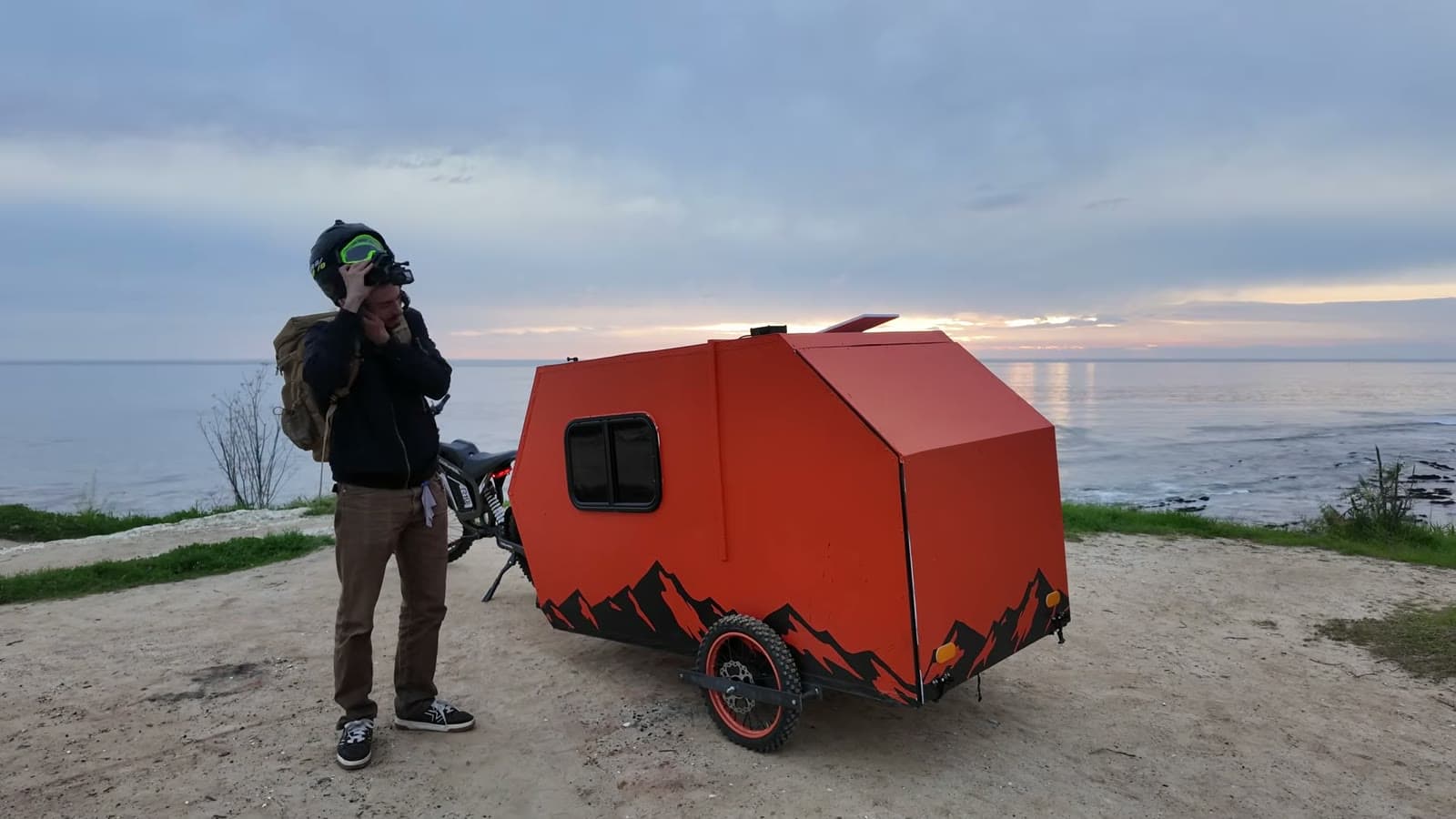 Orange e-bike camper arriving at a sandy bluff above the ocean at dusk