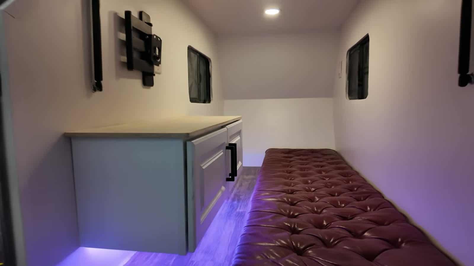 White interior of the e-bike camper with a floating cabinet, purple LED underglow, tufted cushion bed and TV mount