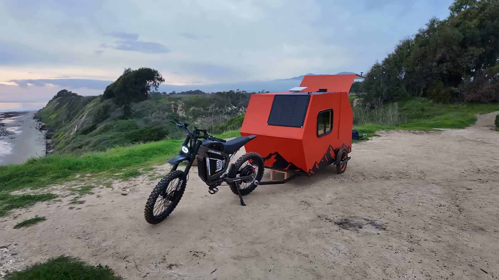 E-bike and orange camper with roof-mounted solar panel parked on a coastal overlook