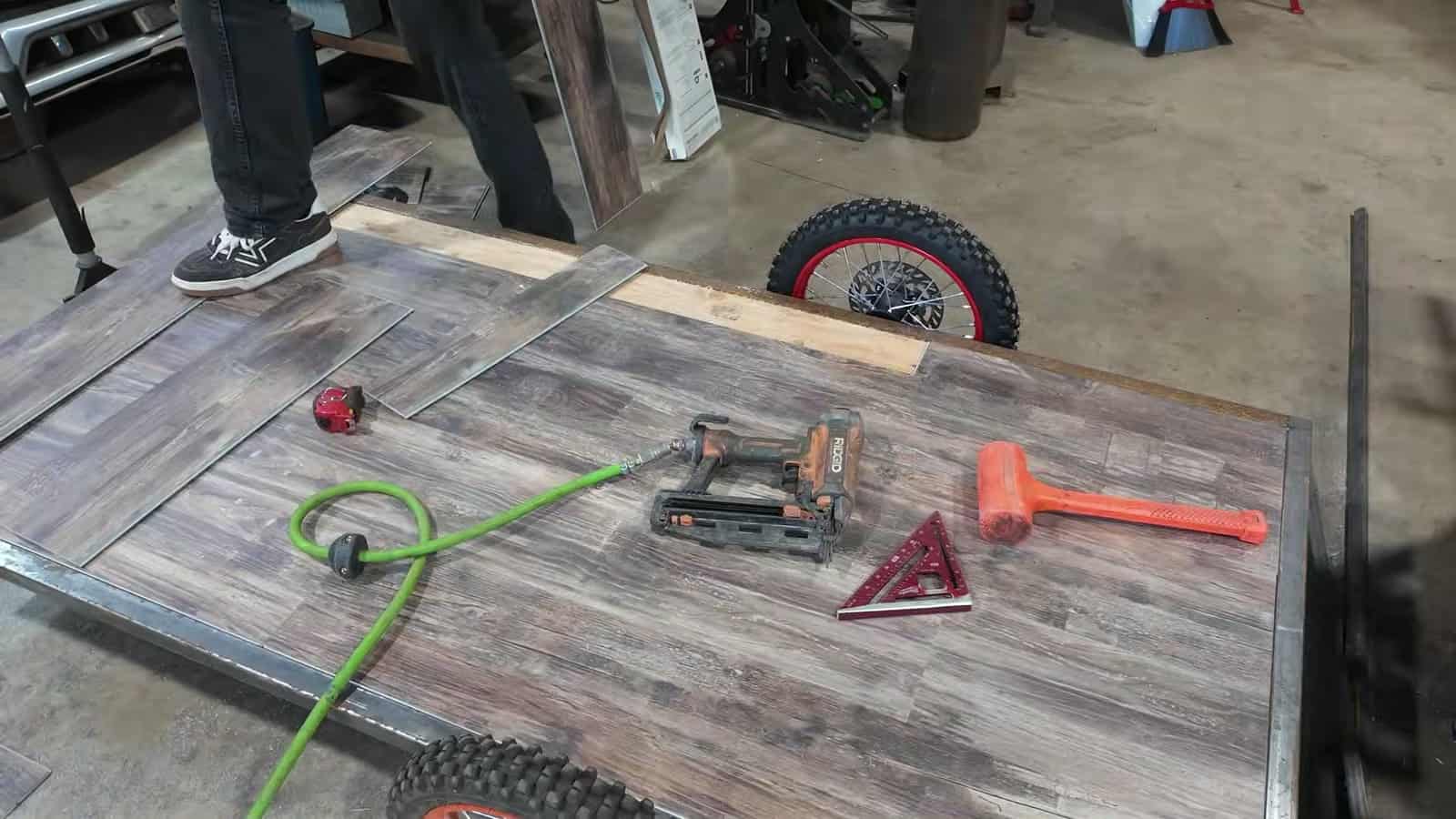 Welded steel trailer frame with plank flooring and red-rimmed e-bike wheels in a workshop