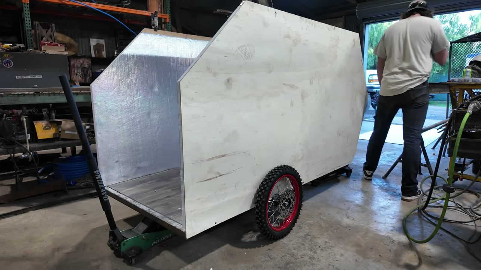 Bare foam-and-wood camper shell on a steel trailer frame inside a workshop