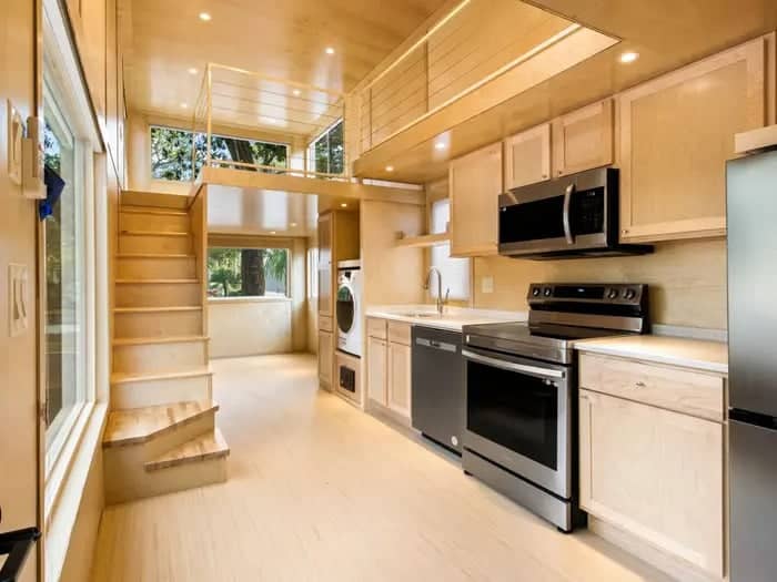 Modern tiny house kitchen with compact appliances and light wood finishes.