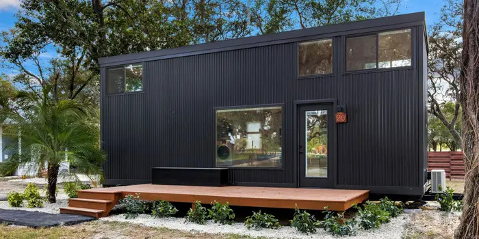 Modern black tiny house with large windows in Tampa Tiny Village setting.