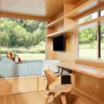 Compact tiny house interior with a bed and workspace overlooking lush greenery.