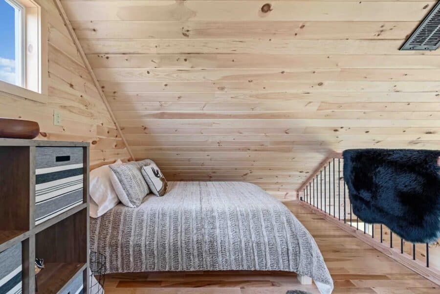 Cozy tiny bedroom with wood-paneled walls and sloped ceiling in Eagles Nest Cabin, West Virginia.