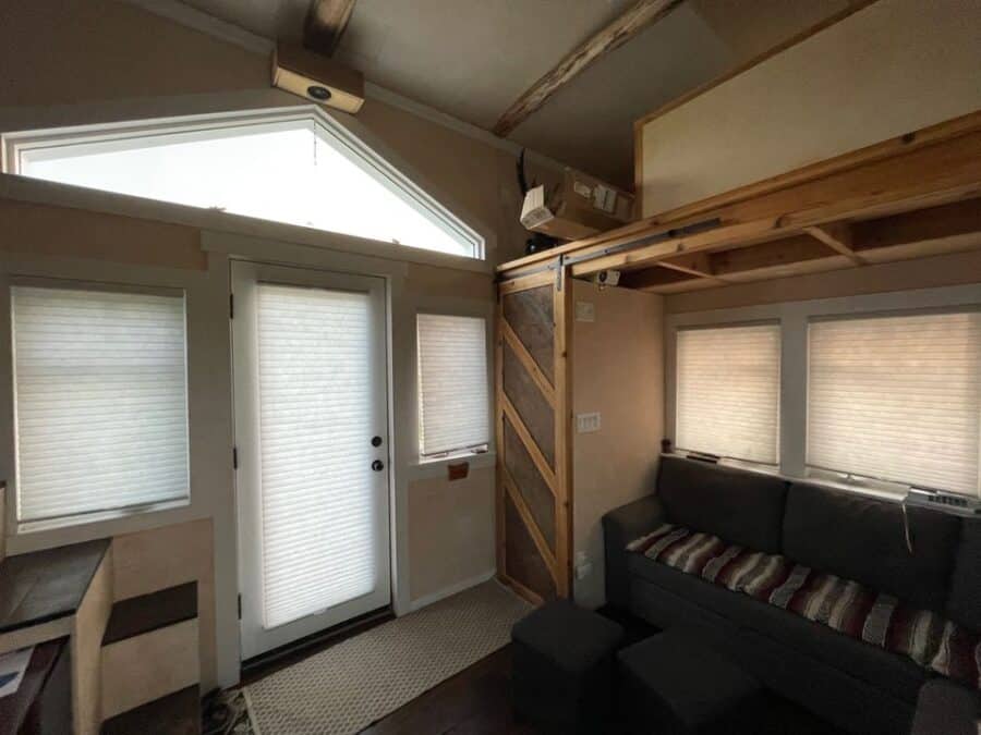 Compact tiny house interior with loft, sofa, and large windows for natural light.