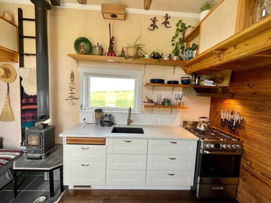 Eco-Bohemian tiny house kitchen with wooden shelves and modern appliances.