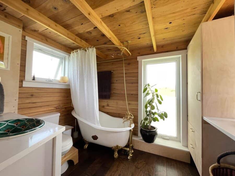 Charming tiny house bathroom featuring a clawfoot bathtub, wooden accents, and ample natural light f.
